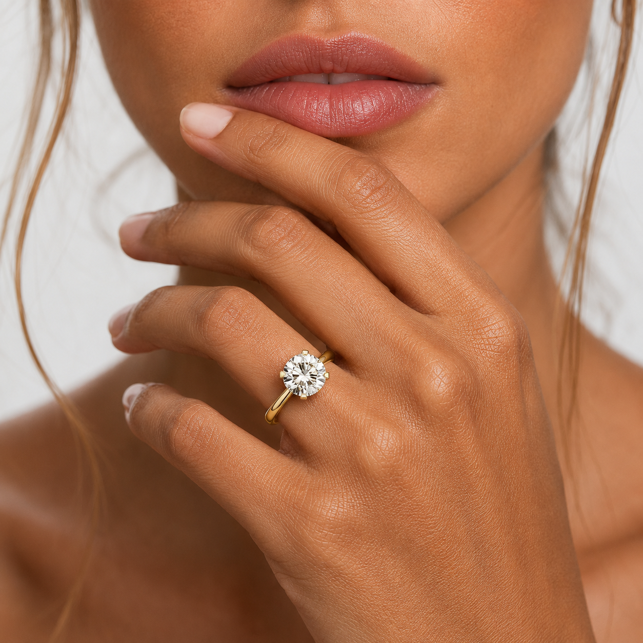 Close-up of a hand wearing a gold ring with a diamond on a neutral background