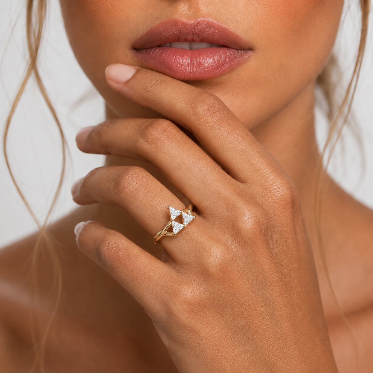 Close-up of a hand wearing a gold ring with a triangular diamond design, against a neutral background.