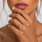 Close-up of a hand wearing a gold ring with a triangular diamond design, against a neutral background.