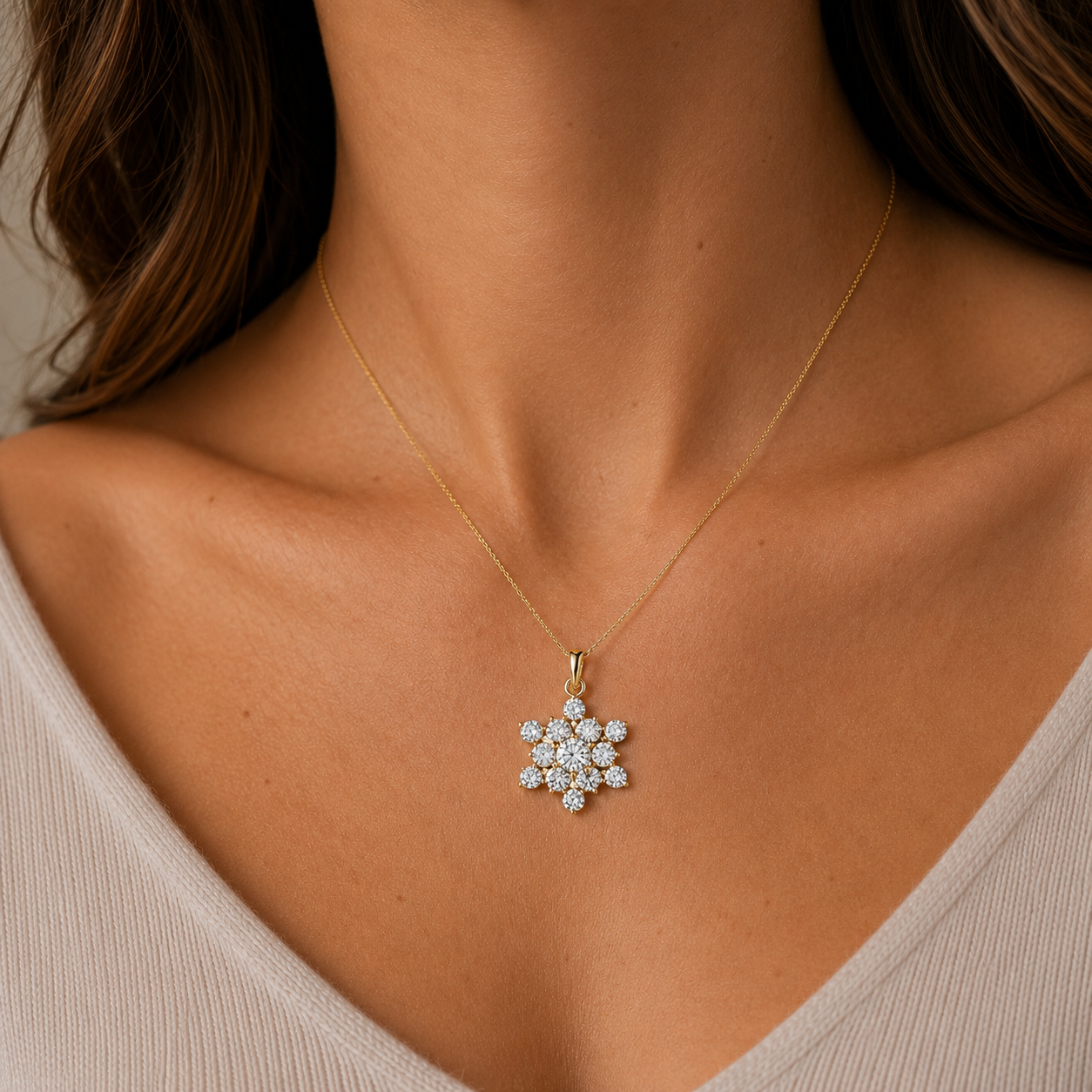 A close-up of a model wearing a delicate gold chain necklace with a snowflake-shaped pendant set with clear stones, styled with a beige ribbed top.