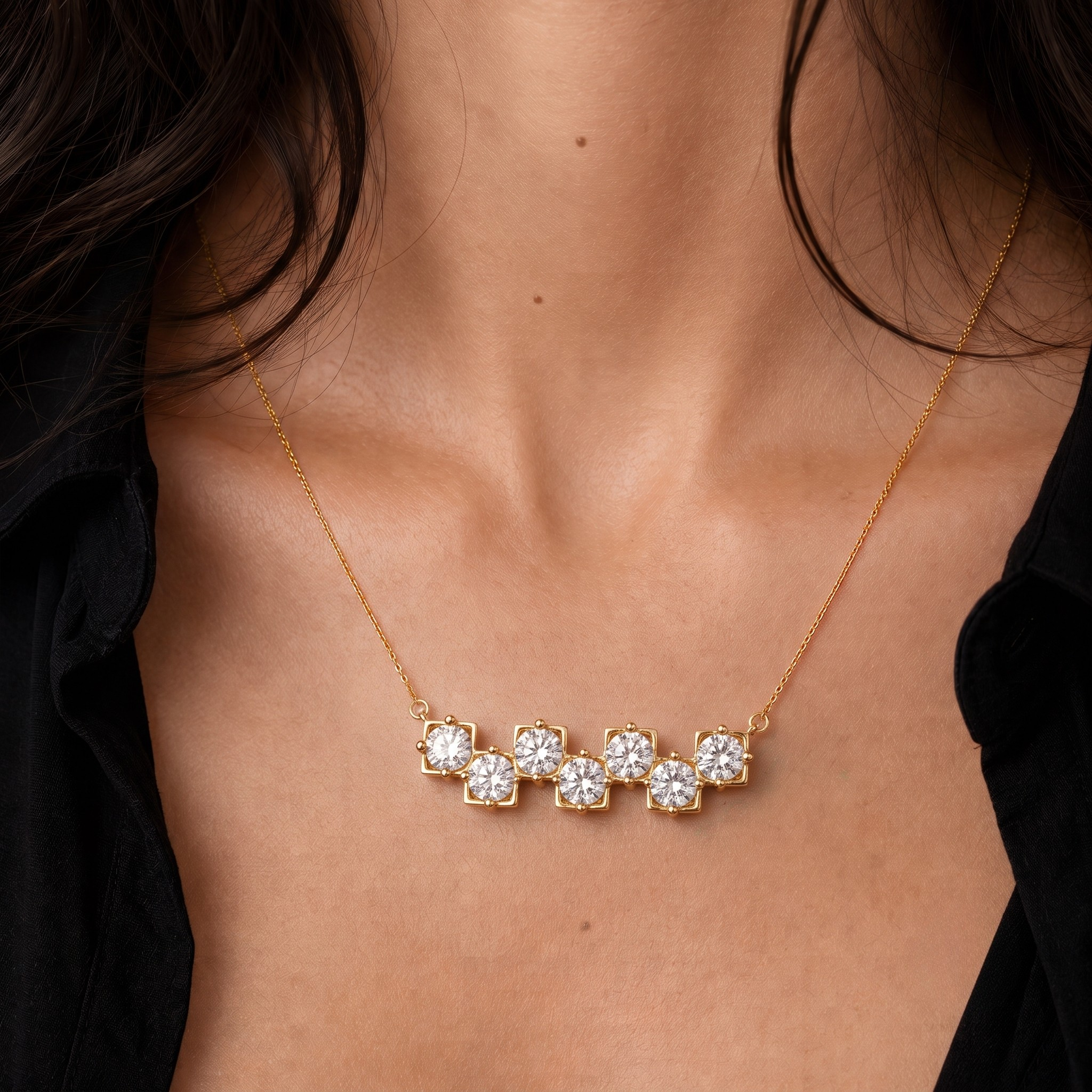 A close-up of a model's neck and chest wearing a delicate gold necklace with five small floral clusters of clear stones set in a row.
